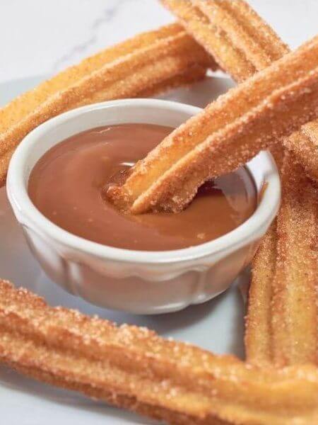 Fertige Churros Rezept auf Gitterrost, ein Churro in heißer Schokolade getaucht