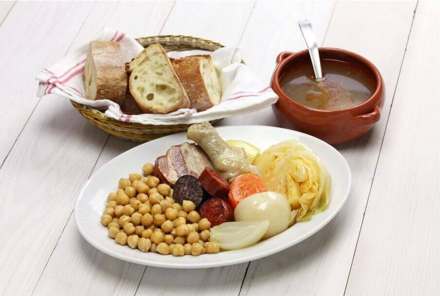 Cocido Madrileño mit Suppe, festen Zutaten und frischem Brot