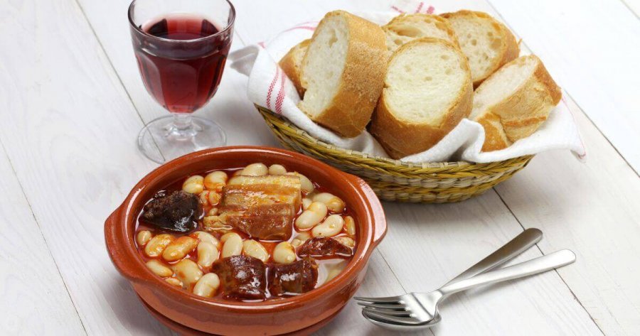 Fabada Asturiana serviert auf dem Tisch mit Wein und frischem Brot, spanisches Eintopf-Rezept